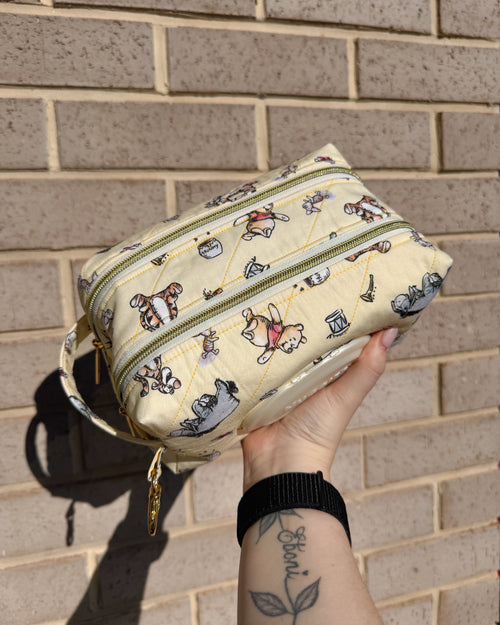 Hand holding a beige pouch with cartoon character patterns against a brick wall.