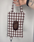 Plaid bag with a circular cutout held by a hand against a gray background