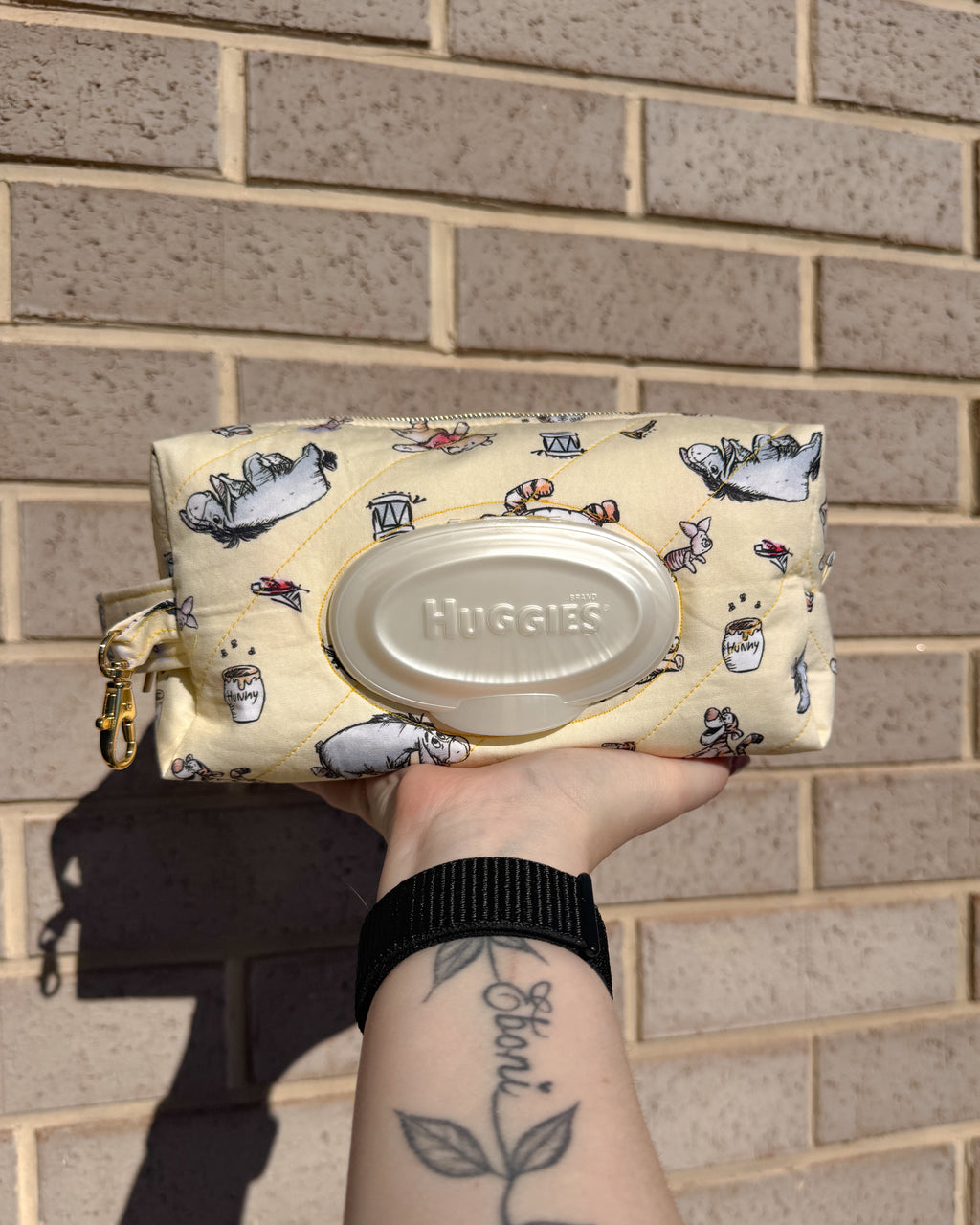 Huggies wipes container in a patterned pouch held against a brick wall