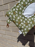 Green fabric pouch with white floral pattern and bee design on a brick wall background