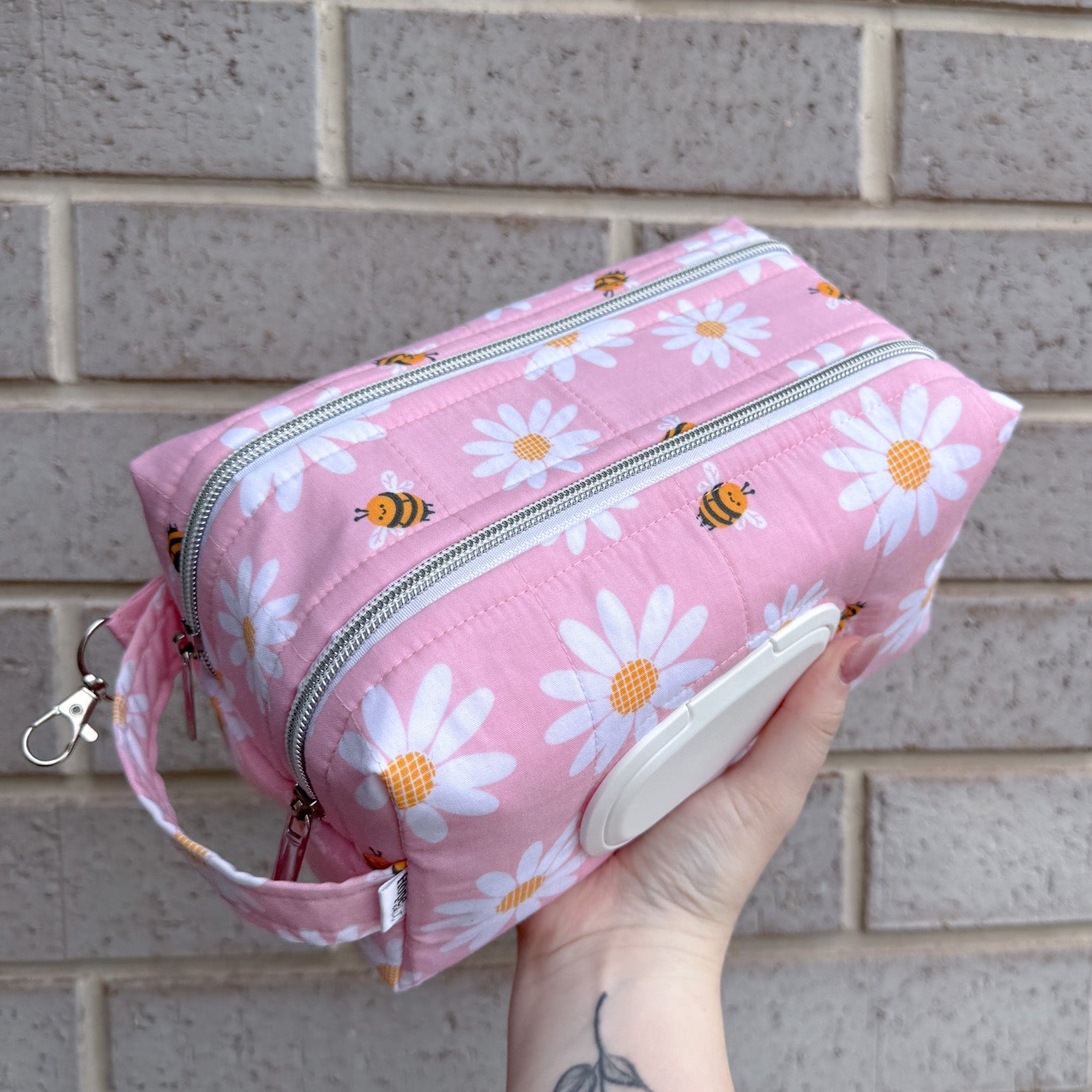 Pink pouch with floral pattern held against a brick wall