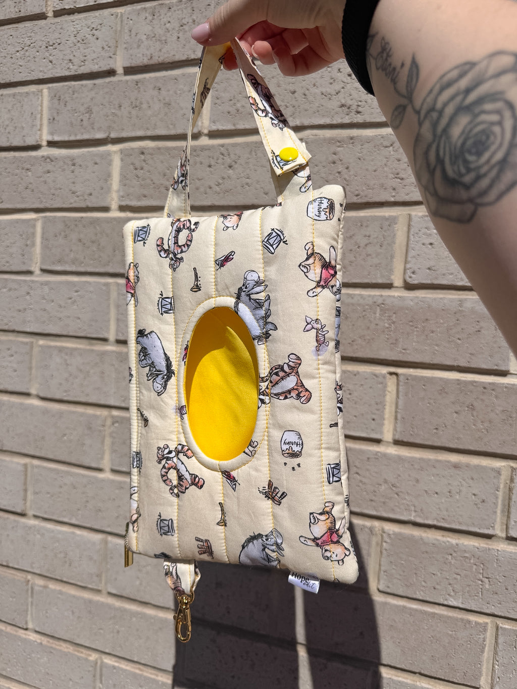 Small pouch with cartoon designs held by a hand against a brick wall.