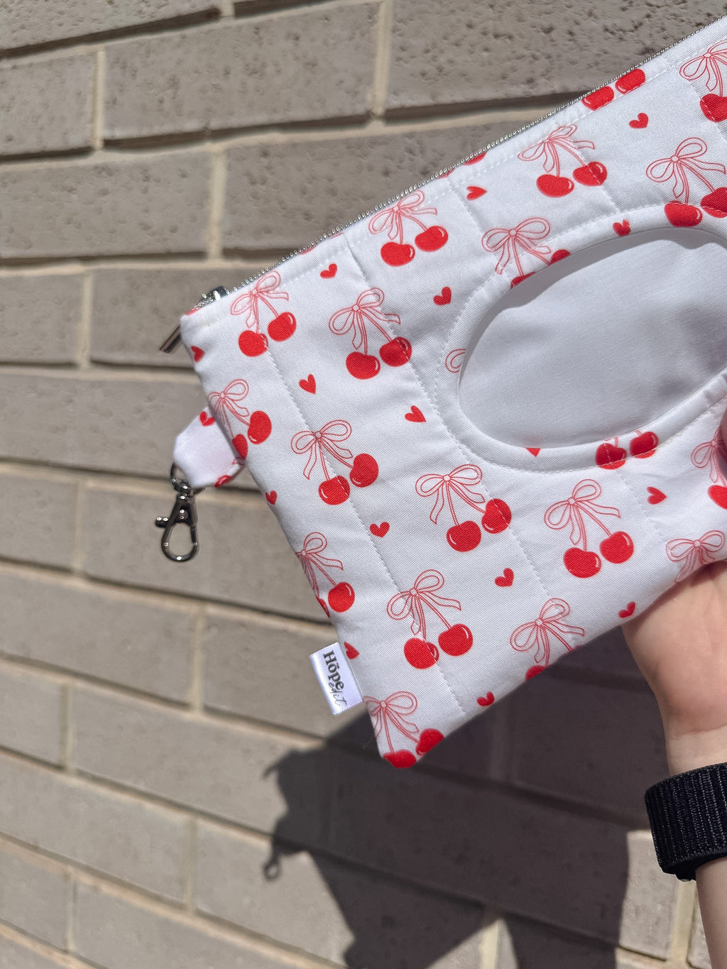 Fabric pouch with red cherry pattern held against a brick wall