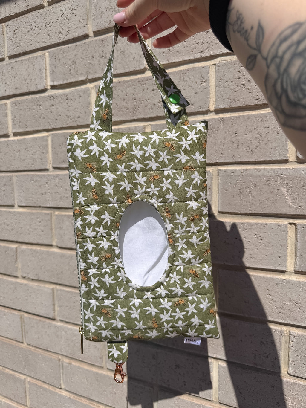 Green fabric bag with white floral pattern held against a brick wall