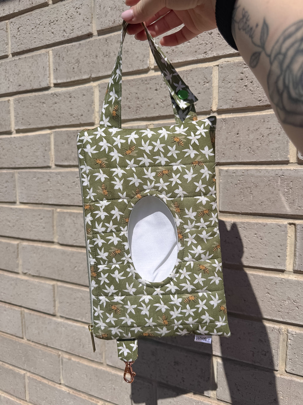 Green fabric bag with white floral pattern held against a brick wall