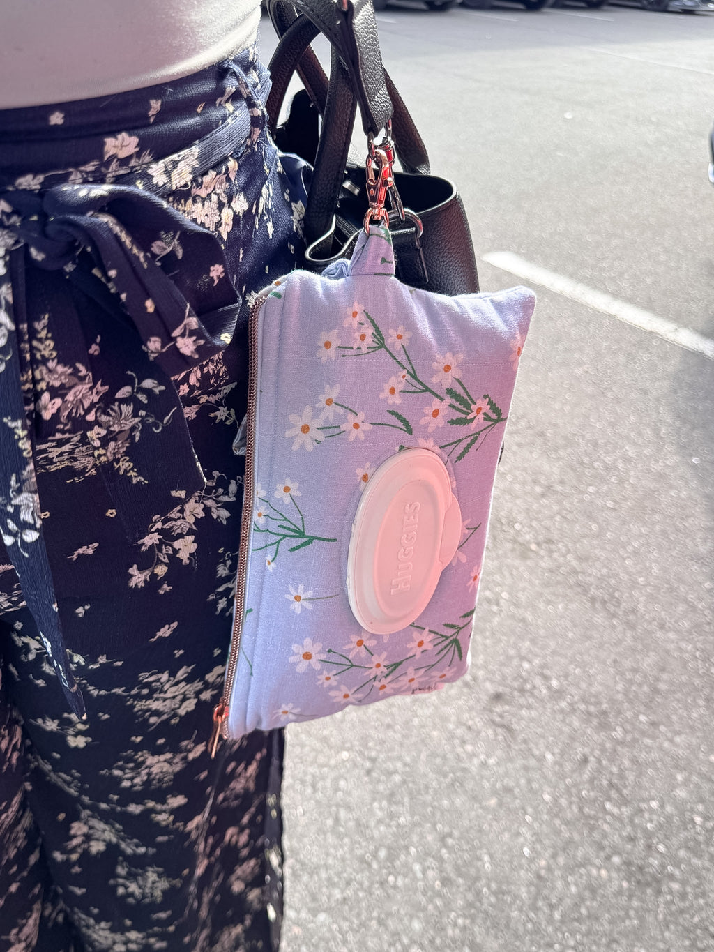 Floral-patterned pouch hanging from a bag on a person's arm with a blurred street background