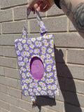 Floral-patterned bag held by a person against a brick wall